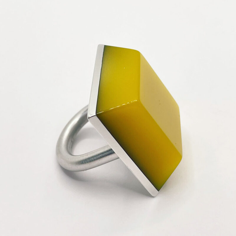 Anello grande ma leggero, composto da una base in alluminio e una finta pietra in resina color giallo, di forma squadrata simile ad una piramide bassa